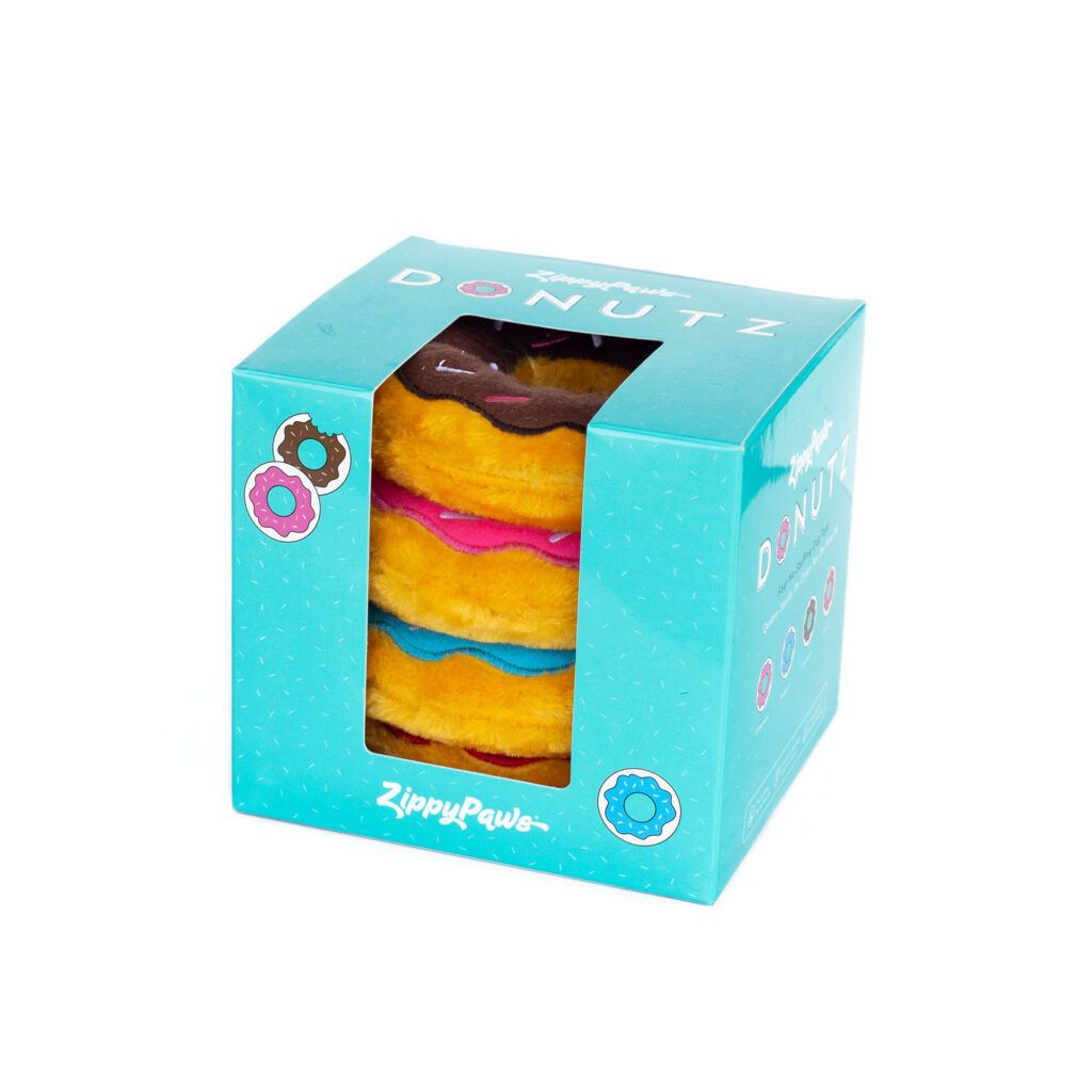 A teal box with a transparent window displays three plush donuts stacked vertically in pink, blue, and yellow colors by ZippyPaws.