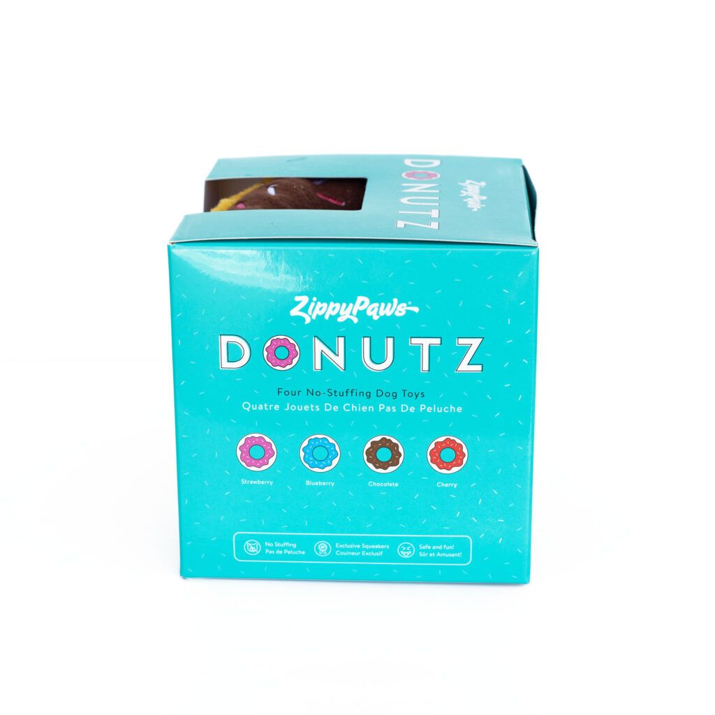 A teal box labeled "ZippyPaws DONUTZ" containing four no-stuffing dog toys designed to resemble donuts, in strawberry, blueberry, chocolate, and cherry flavors.