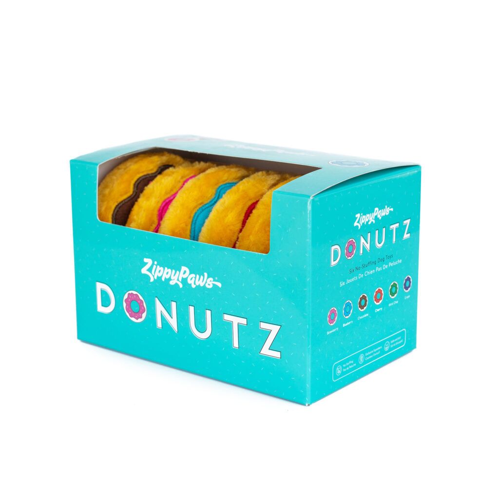 A teal ZippyPaws Donutz box contains colorful plush dog toys shaped like donuts, with a clear plastic window displaying the toys inside.