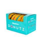 A teal ZippyPaws Donutz box contains colorful plush dog toys shaped like donuts, with a clear plastic window displaying the toys inside.