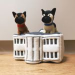 Two Zippy Burrow® - Champ and Major, one with a red collar and the other with a blue collar, sit on top of a white, plush toy structure resembling a building, placed on a wooden floor against a plain background.