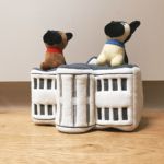 Two "Zippy Burrow® - Champ and Major," one with a red collar and the other with a blue collar, sit on top of a white and gray plush structure with windows. The scene is set on a wooden floor against a plain background.