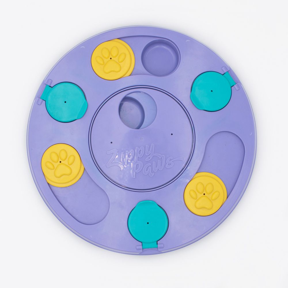 A SmartyPaws Puzzler Purple circular dog puzzle toy with yellow paw print sliders and blue covers. The brand name "Zippy Paws" is embossed in the center.