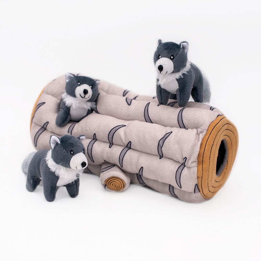 Three grey and white wolf plush toys are positioned on and around a Zippy Burrow® - Arctic Wolf, which is designed to resemble a cut section of a tree log.