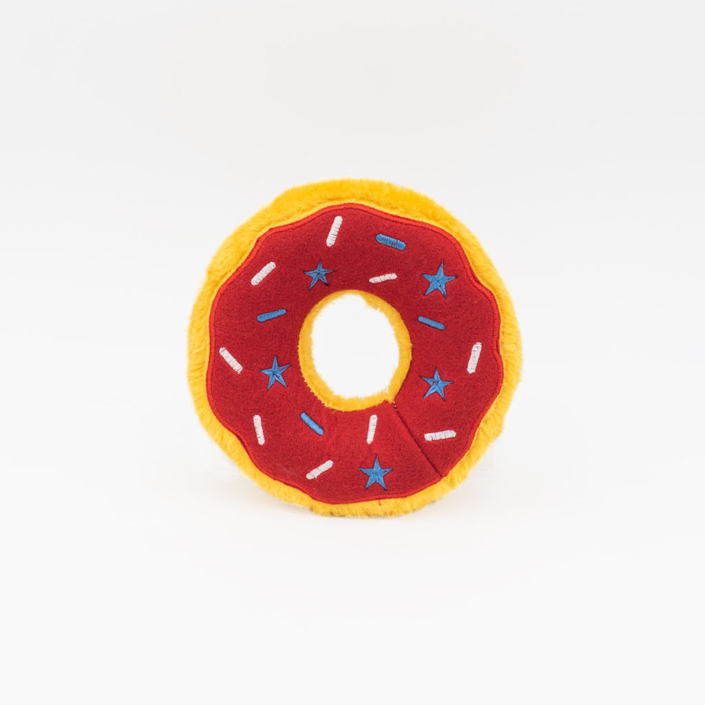 A round, plush Donutz - Americana toy with a red center, yellow edge, blue stars, and white sprinkles against a white background.