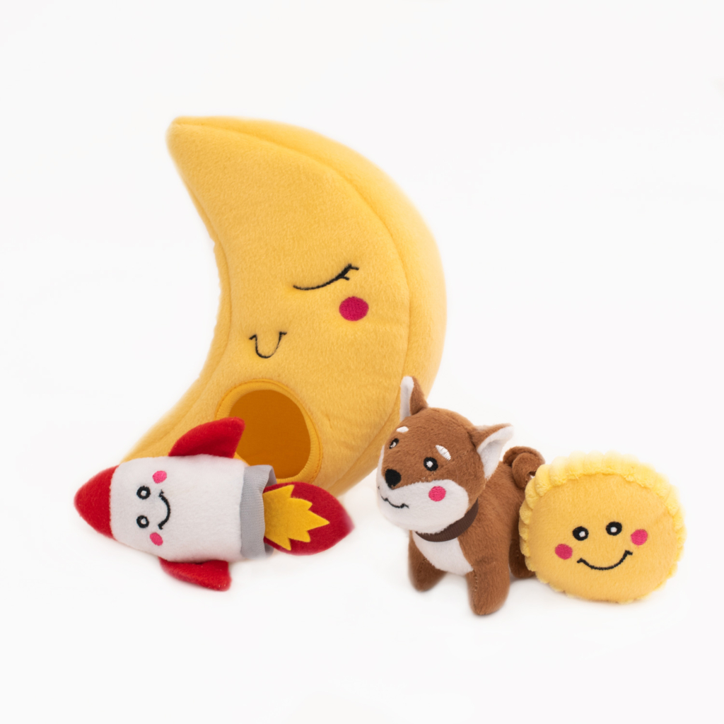 A Zippy Burrow® - To the Moon set featuring a smiling crescent moon with a hole, accompanied by three smaller plush toys: a rocket, a fox, and a smiling round cheese.