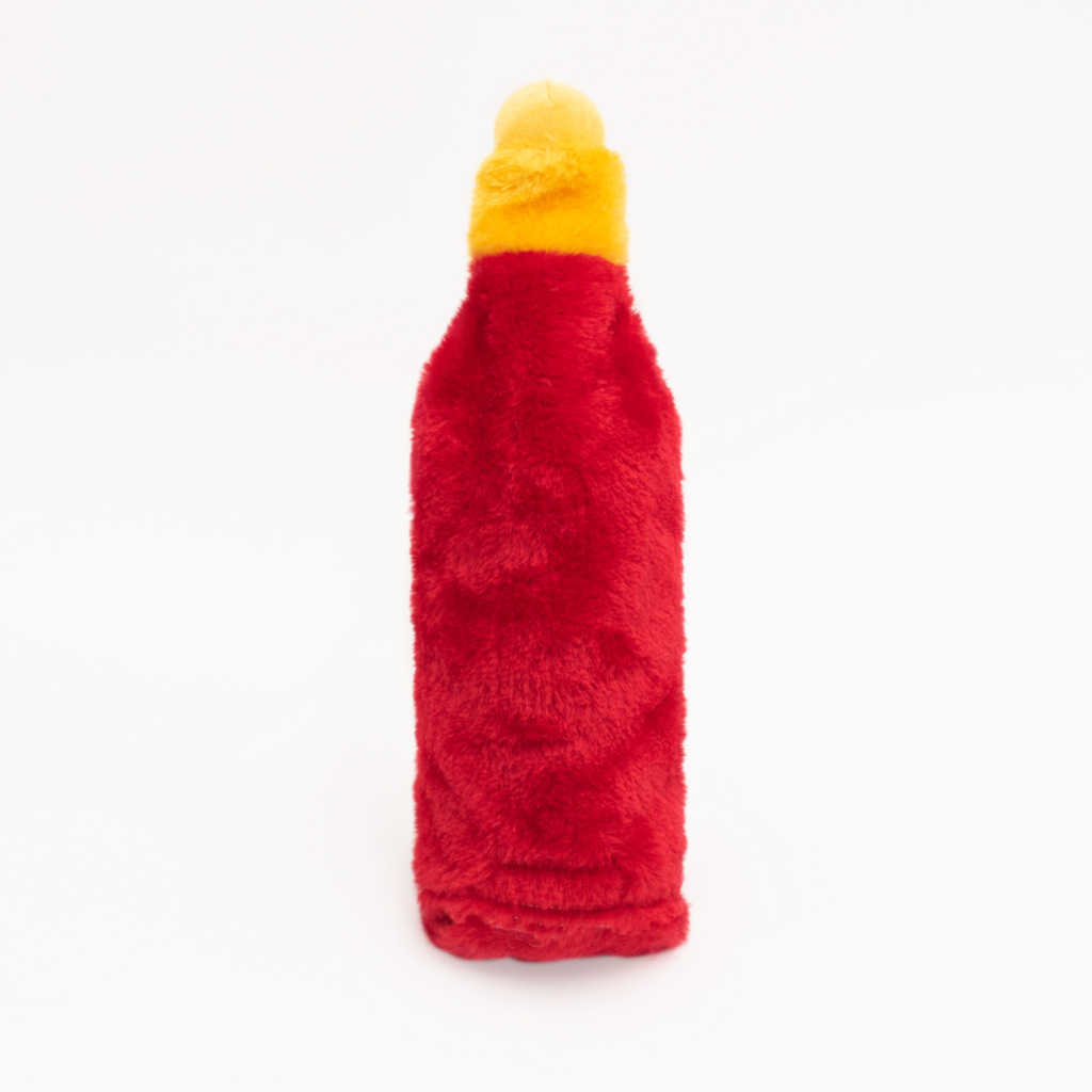 A plush toy designed to resemble a hot sauce bottle with a red body and yellow cap, standing upright on a white background.