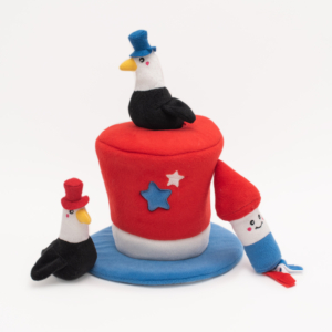 The Zippy Burrow® - Americana Top Hat features three plush toys: two eagles wearing top hats and a smiling firework, around and on a red, white, and blue-themed cylindrical cushion adorned with stars, on a blue circular base.