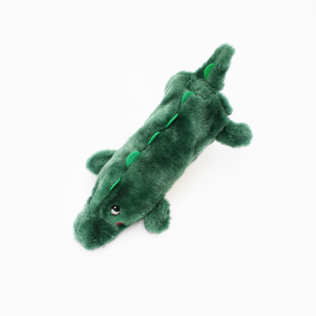 A green plush toy designed to resemble a crocodile, featuring small limbs, ridges along the back, and two eyes. It is placed against a plain white background.