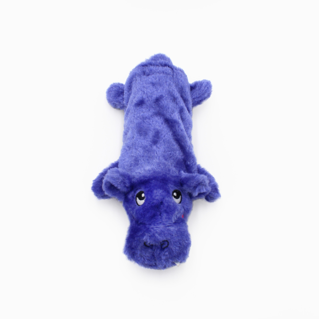 A plush toy shaped like a hippo lies on its stomach. The toy is purple with a smooth texture and features embroidered eyes and mouth on its face.