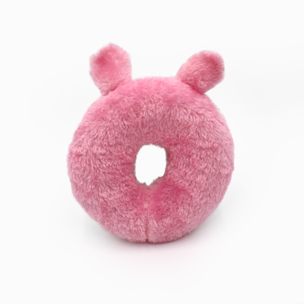 A pink, round plush toy with a hole in the center and two small ears at the top.