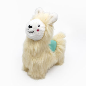 A soft, cream-colored llama plush toy with a smiling face and rosy cheeks, featuring a small green patch on its back.