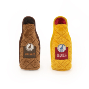 Two plush toys resembling bottles, one brown with "Whiskey" and one yellow with "Tequila" labels embroidered on their fronts, are standing side by side on a plain white background as part of the Z-Stitch® Happy Hour Crusherz 2-Pack - Whiskey and Tequila.