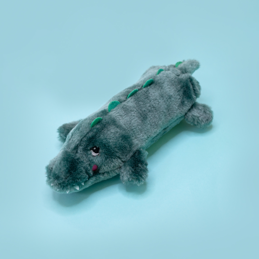 A small, grey and green Bottle Crusherz - Alligator lying on a light blue background.