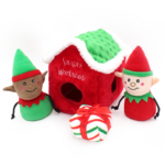 Plush toy set featuring two elf dolls, a red and green 'Holiday Burrow® - Santa's Workshop' house, and a white, green, and red striped gift with a bow.