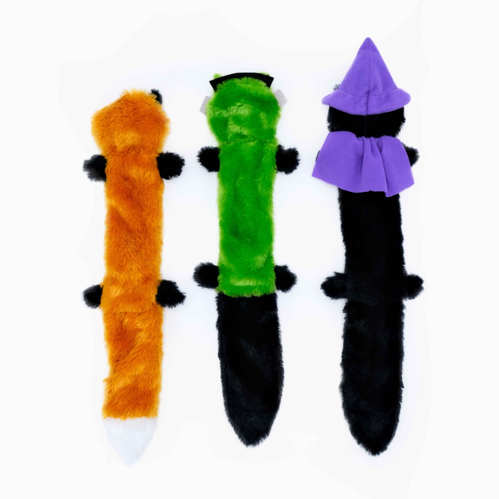 Three Halloween Skinny Peltz 3-Pack Large, each resembling a long, fuzzy creature in different colors (orange, green, and black) with various hat and cape accessories, arranged side-by-side.
