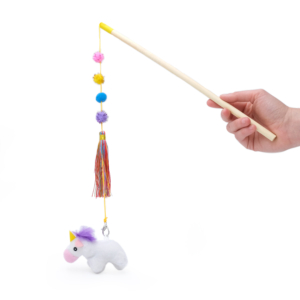 A hand holds a ZippyClaws® ZippyStick - Unicorn consisting of a wooden rod with a string attached, dangling a white plush unicorn, colorful pom-poms, and tassels.