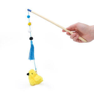 A hand holds a wooden stick with a string attached to a fluffy yellow chick toy, blue tassels, and colorful pom-poms, used as the ZippyClaws® ZippyStick - Bird.