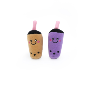 Two plush toys resembling bubble tea drinks with cute, smiling faces. One is brown with a pink straw and black pearls, while the other is purple with a pink straw and black pearls. The background is plain white. Product Name: ZippyClaws® NomNomz® - Milk Tea and Taro