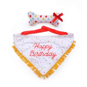 A white **Birthday Bandana and Bone 2-Pack** with "Happy Birthday" in red text, adorned with yellow fringe and multicolored dots, is paired with a stuffed bone toy featuring polka dots and a red ribbon bow.