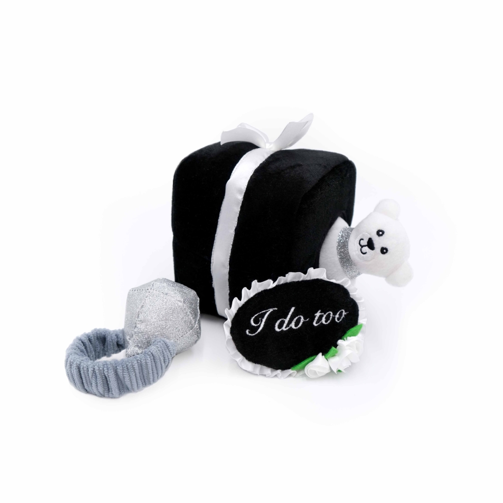 A Zippy Burrow® - Wedding Ring Box with a white ribbon, accompanied by a gray ring, a white bear plush, and a black sign reading 