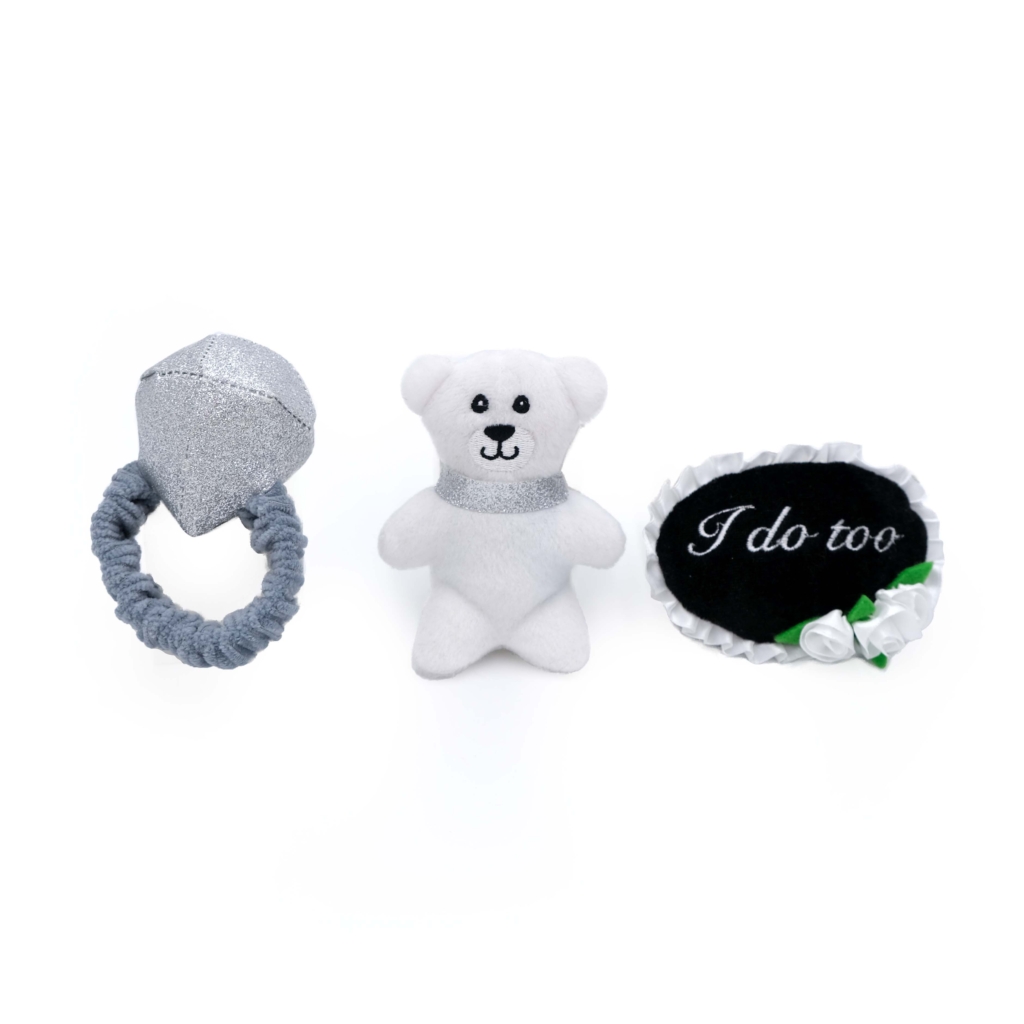 Three **Zippy Burrow® - Wedding Ring Box** baby toys are seen: a soft, silver ring, a white teddy bear, and an oval-shaped rattle with 