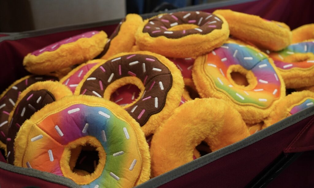A pile of plush toy donuts with colorful icing and sprinkles, displayed in a red container.