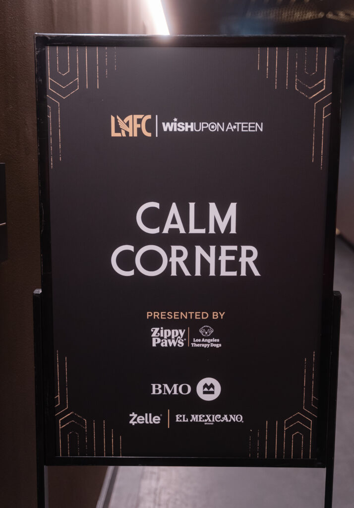 A black sign titled “Calm Corner” presented by LMFC, Wish Upon A Teen, ZippyPaws, Los Angeles Therapy Dogs, BMO, Zelle, and El Mexicano.
