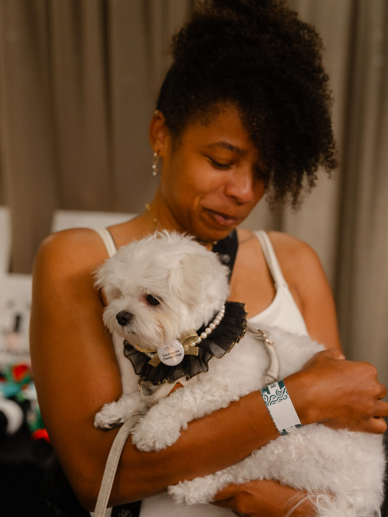 A woman holding a small white dog wearing a ruffled collar with a “Los Angeles Therapy Dogs” pin.