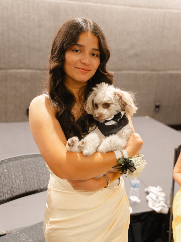 A young woman holding a small, light-colored dog wearing a black bow tie.
