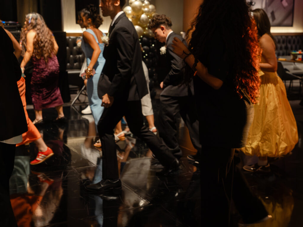 People in formal attire walking across a dark, reflective dance floor at an event.