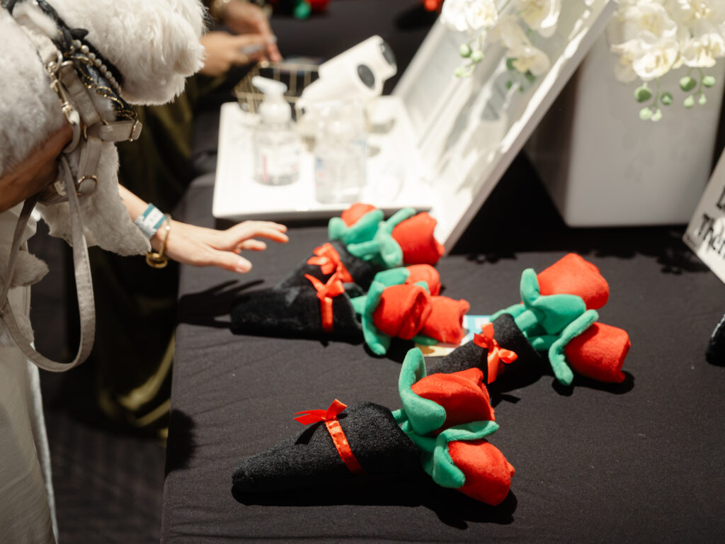A person’s hand reaches toward plush rose-shaped toys with black fabric bases on a table.